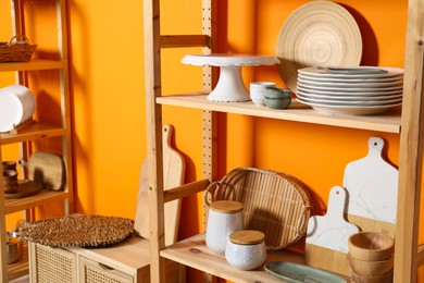 Photo of Wooden storage stands and cabinet with kitchenware near orange wall indoors