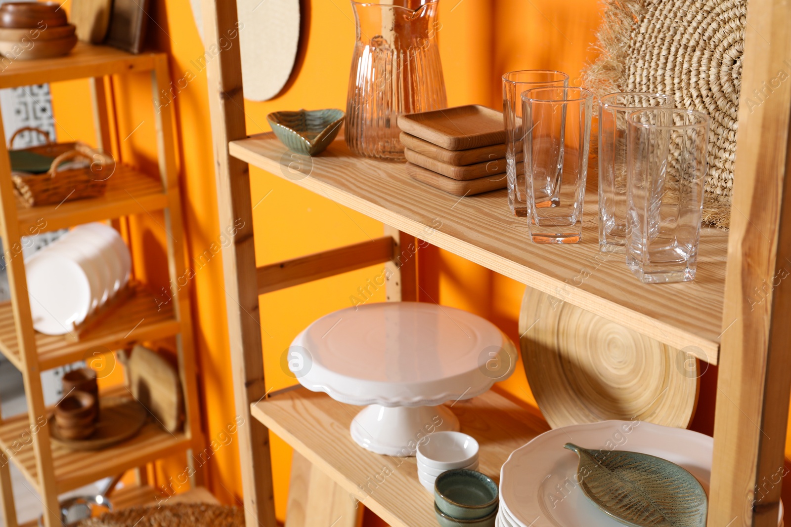 Photo of Wooden storage stands with kitchenware near orange wall indoors, closeup