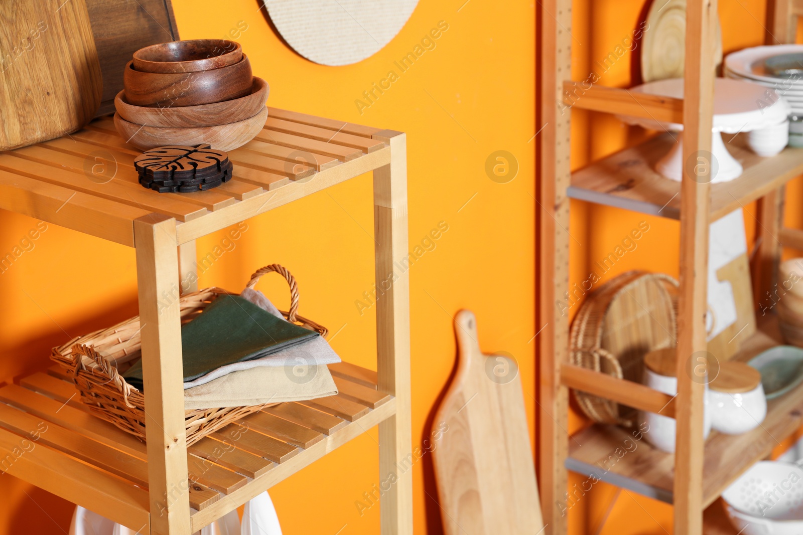 Photo of Wooden storage stands with kitchenware near orange wall indoors, closeup