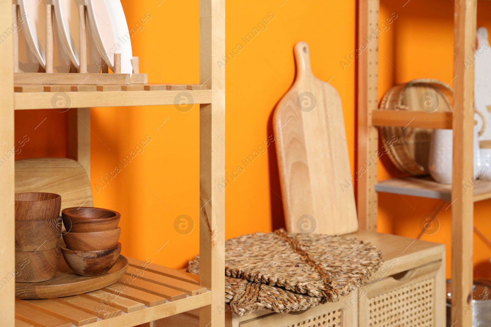 Photo of Wooden storage stands and cabinet with kitchenware near orange wall indoors