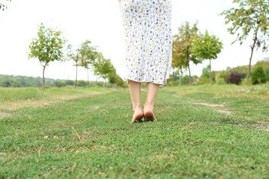 Photo of Woman walking barefoot on green grass outdoors, closeup