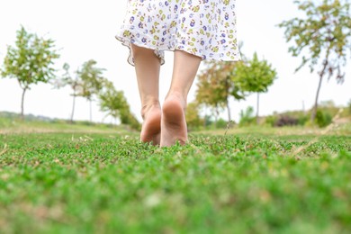 Photo of Woman walking barefoot on green grass outdoors, closeup