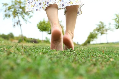 Photo of Woman walking barefoot on green grass outdoors, closeup