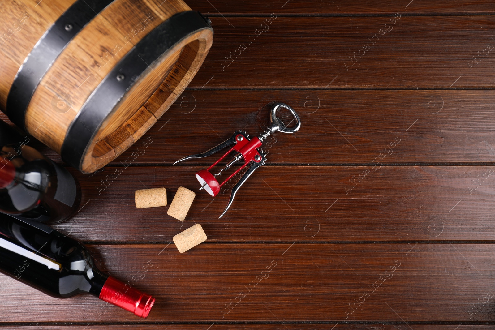 Photo of Wing corkscrew, corks, bottles of wine and barrel on wooden table, top view. Space for text