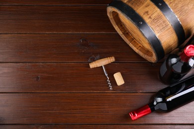 Photo of Corkscrew, cork, bottles of wine and barrel on wooden table, top view. Space for text