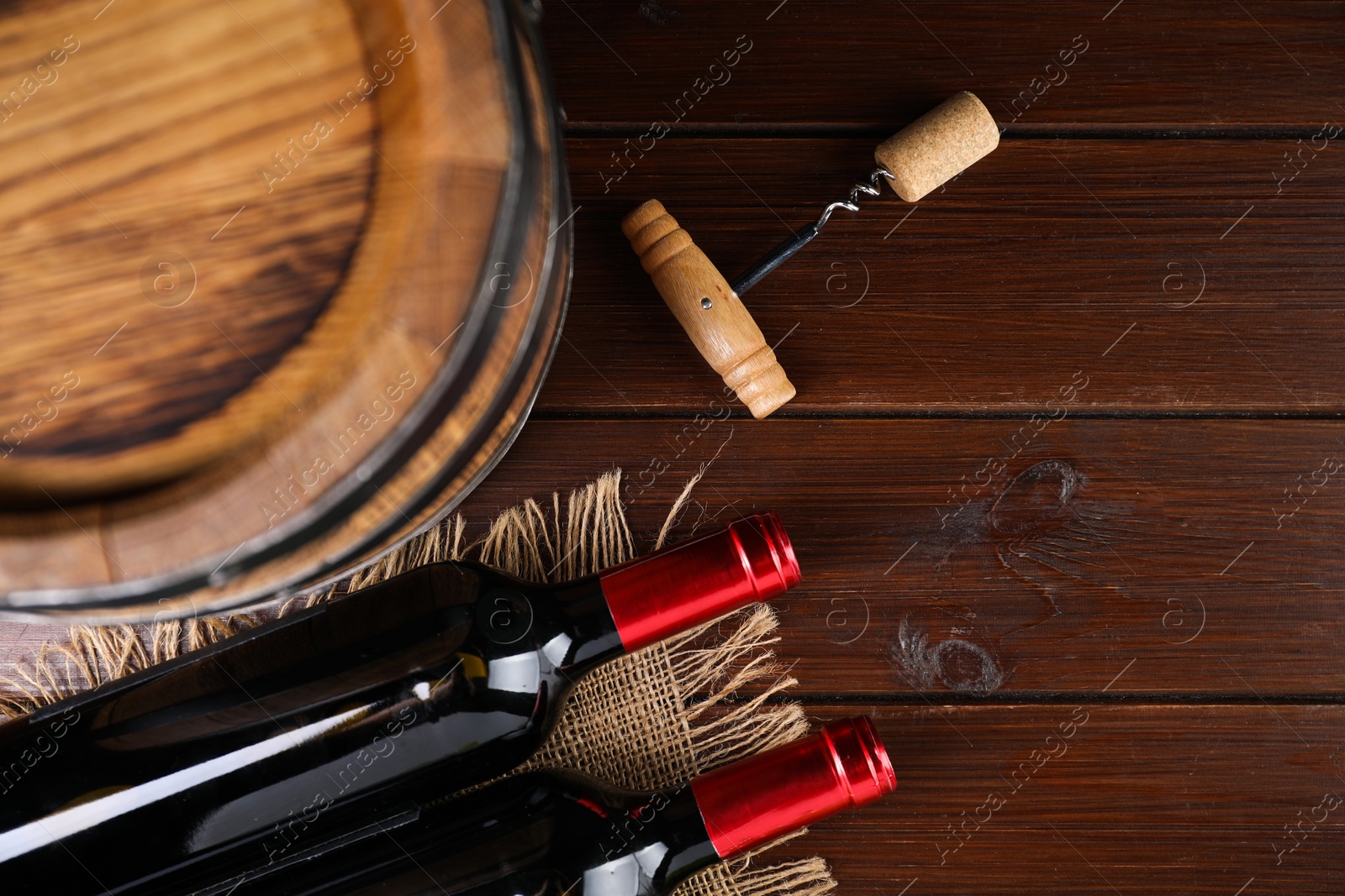 Photo of Corkscrew, cork, bottles of wine and barrel on wooden table, top view. Space for text