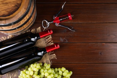 Photo of Wing corkscrew, bottles of wine, grapes and barrel on wooden table, top view. Space for text