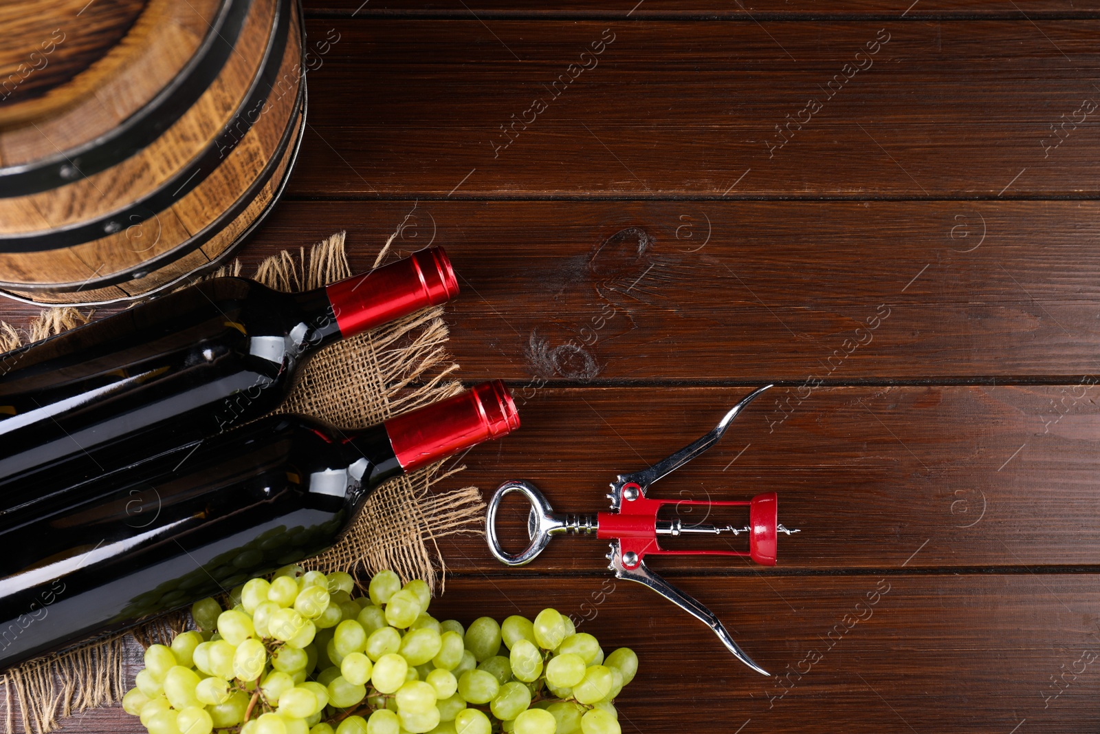 Photo of Wing corkscrew, bottles of wine, grapes and barrel on wooden table, top view. Space for text