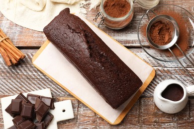 Photo of Tasty chocolate sponge cake and ingredients on wooden table, flat lay