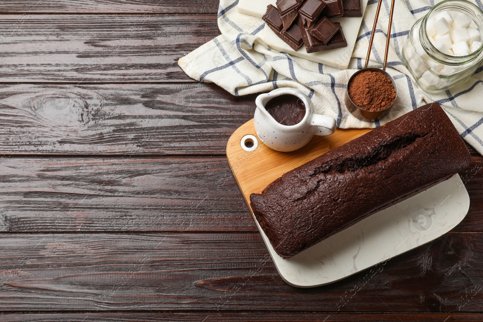 Photo of Tasty chocolate sponge cake and ingredients on wooden table, flat lay. Space for text