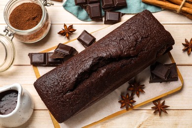 Photo of Tasty chocolate sponge cake and ingredients on white wooden table, flat lay