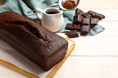 Photo of Tasty chocolate sponge cake and ingredients on white wooden table, closeup