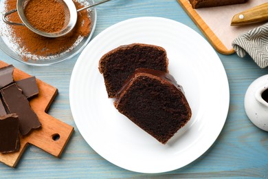 Photo of Tasty sponge cake, pieces of chocolate and cocoa powder on light blue wooden table, top view