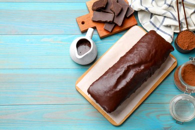 Photo of Tasty chocolate sponge cake and ingredients on light blue wooden table, top view. Space for text