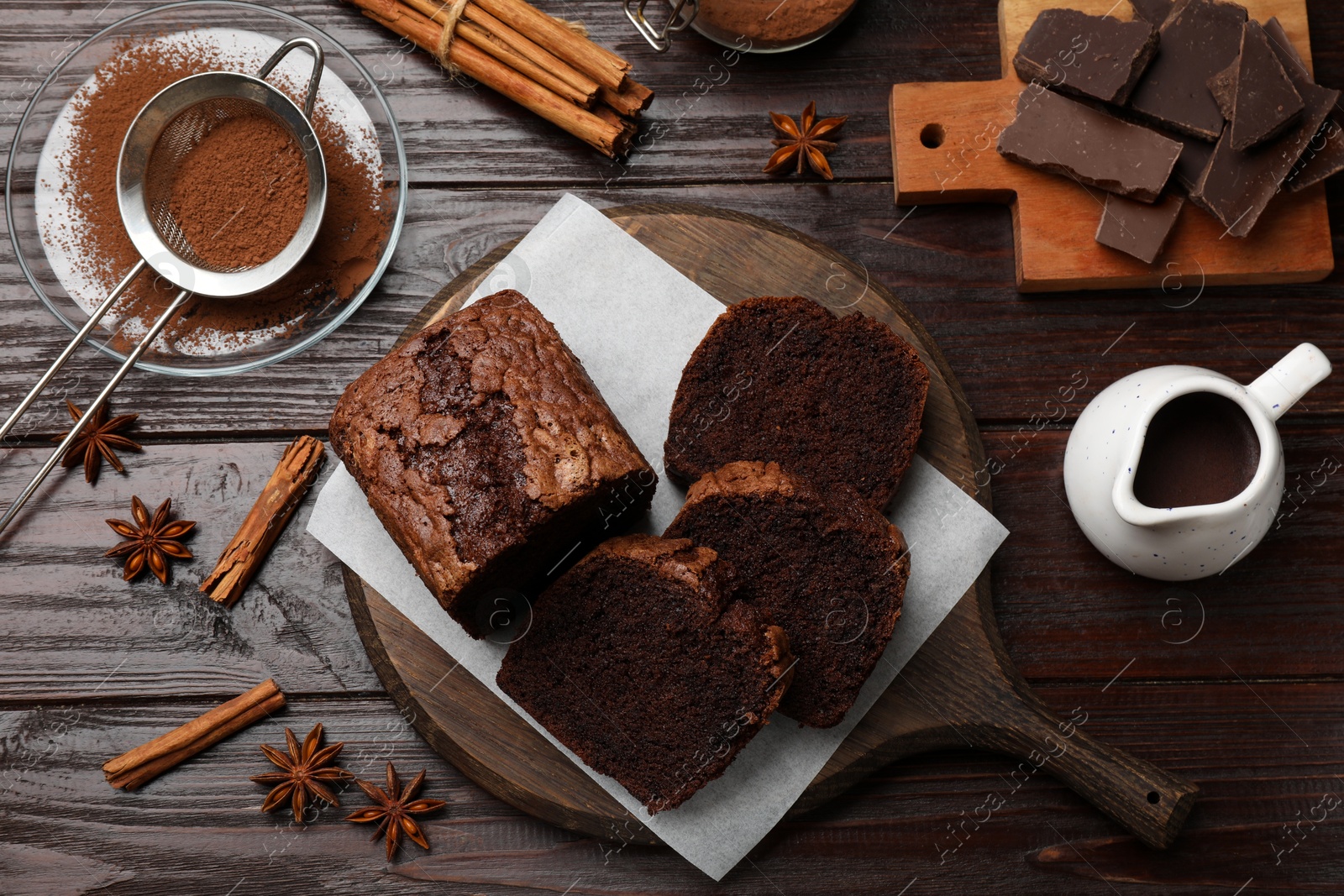 Photo of Delicious cut chocolate sponge cake and ingredients on wooden table, flat lay