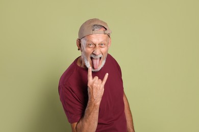 Photo of Portrait of emotional senior man showing rock gesture on green background