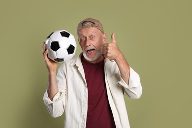 Photo of Portrait of emotional senior man with soccer ball showing thumbs up on green background