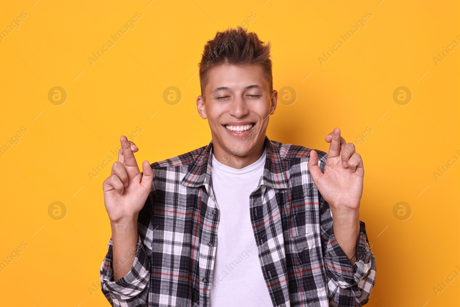 Photo of Excited young student crossing fingers on yellow background. Hope for good exam result