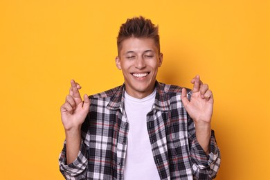 Excited young student crossing fingers on yellow background. Hope for good exam result