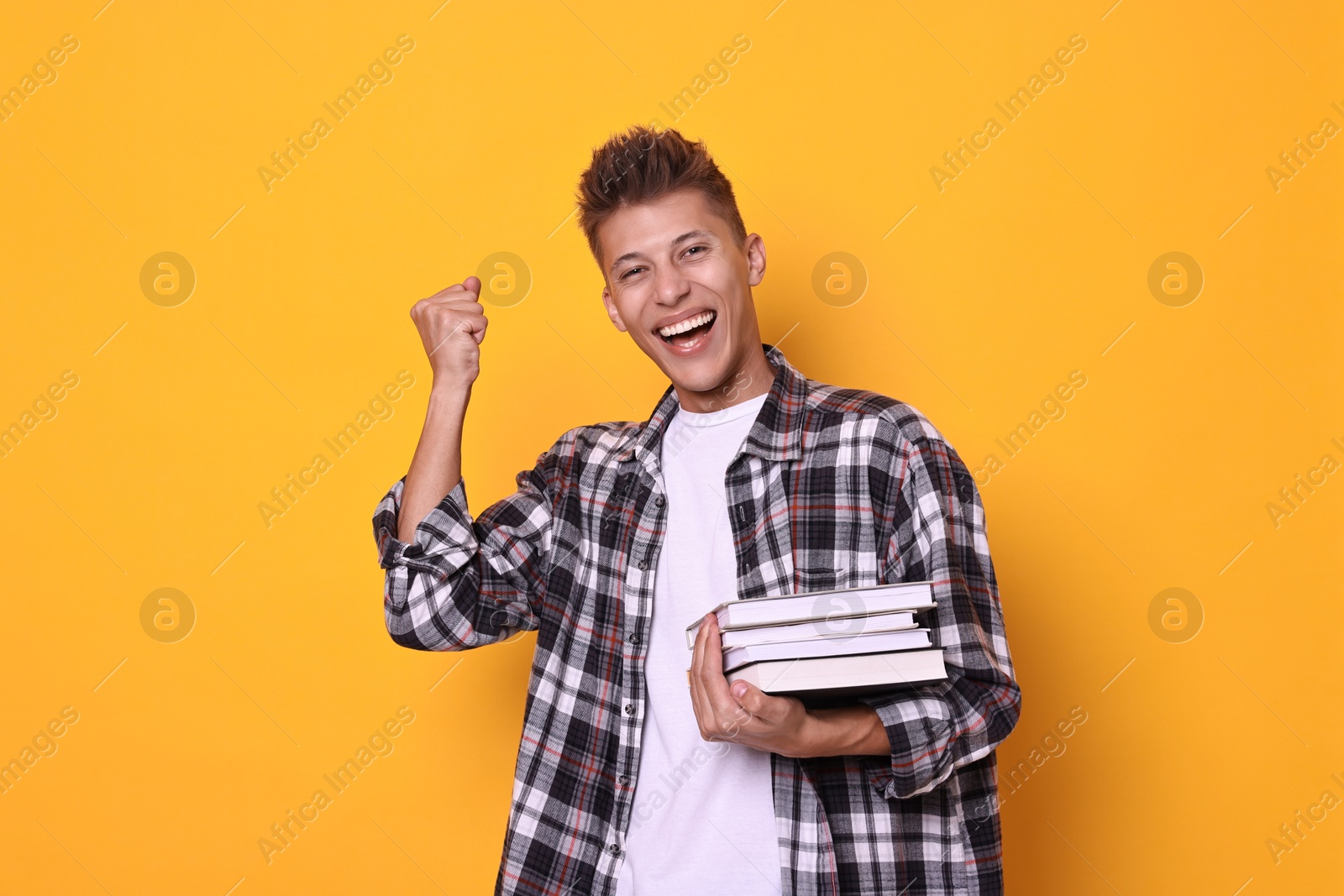 Photo of Young student with stack of books happy about his good exam result on yellow background