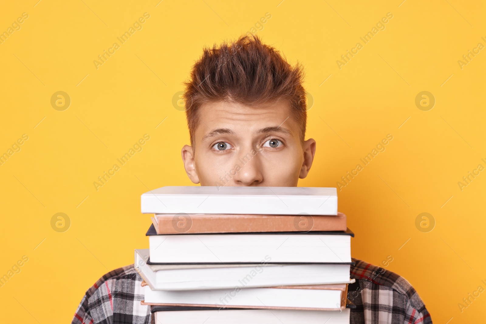 Photo of Young student with stack of books having stress before exam on yellow background, closeup