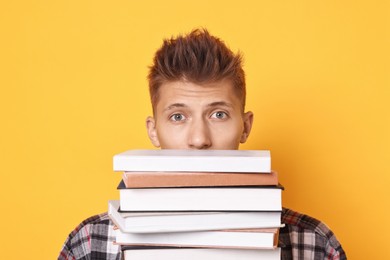 Photo of Young student with stack of books having stress before exam on yellow background, closeup