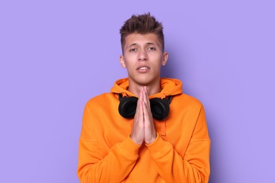 Young student praying for good exam result on violet background