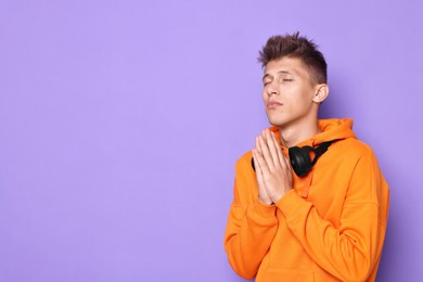 Young student praying for good exam result on violet background, space for text