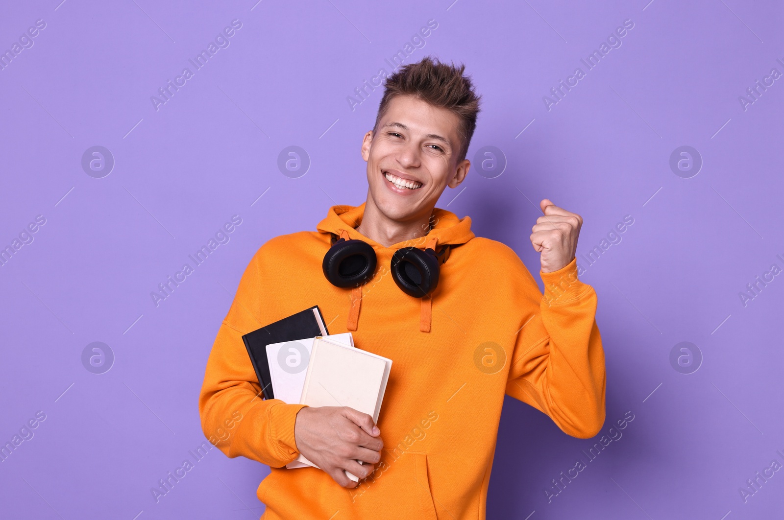 Photo of Young student with books happy about his good exam result on violet background