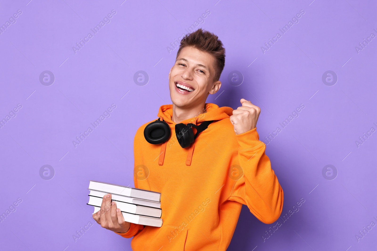 Photo of Young student with stack of books happy about his good exam result on violet background