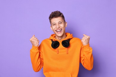 Happy young student with headphones on violet background