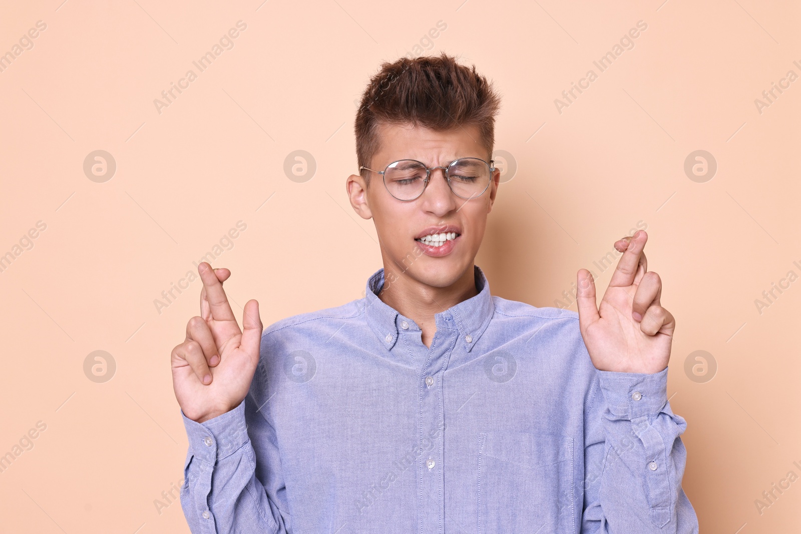 Photo of Emotional young student crossing fingers on beige background. Hope for good exam result