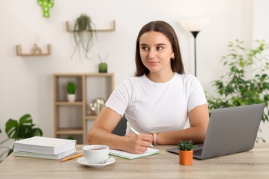 Photo of Student taking notes while studying at wooden table indoors