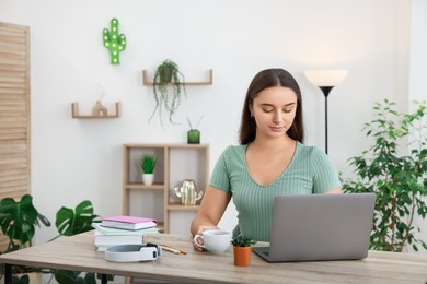 Photo of Student with cup of drink studying at wooden table indoors