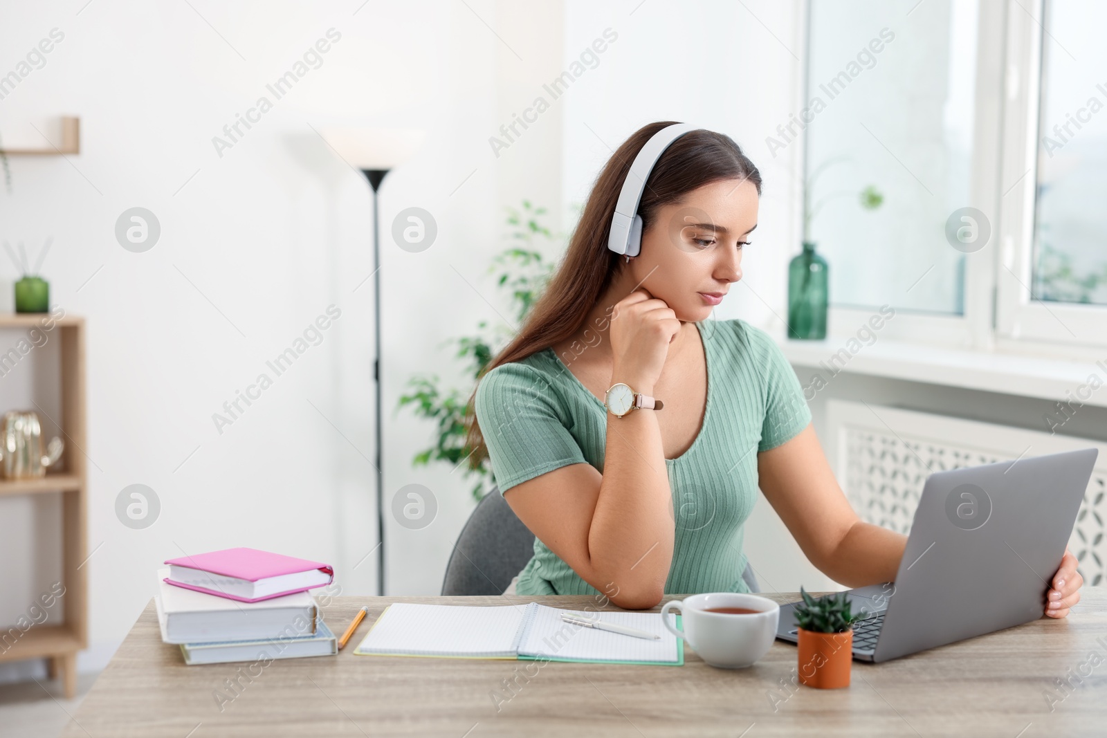 Photo of Student in headphones studying at wooden table indoors