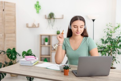 Photo of Student in headphones studying with laptop at wooden table indoors