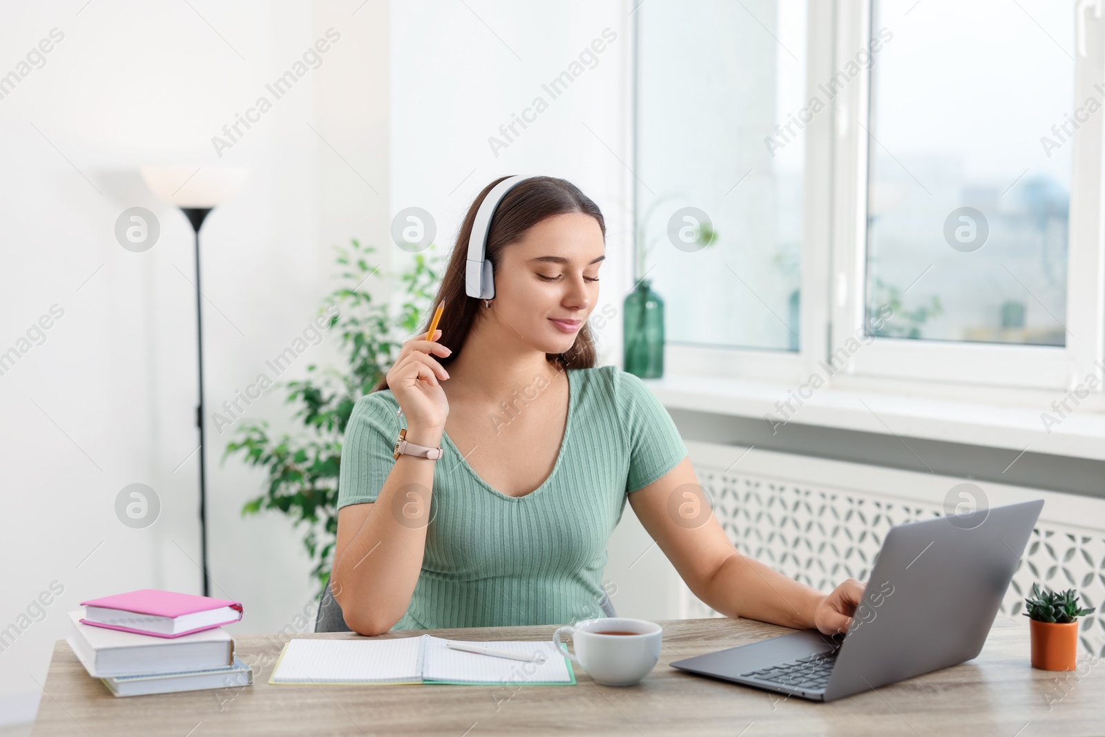 Photo of Student in headphones studying with laptop at wooden table indoors