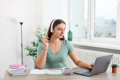 Student in headphones studying with laptop at wooden table indoors