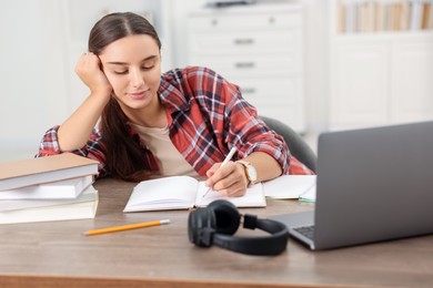 Photo of Student taking notes while studying at wooden table indoors