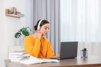 Student in headphones studying with laptop at wooden table indoors