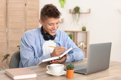 Student with headphones studying at wooden table indoors