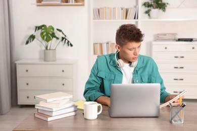 Photo of Student with headphones studying at wooden table indoors