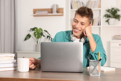 Student with headphones and cup of drink studying at wooden table indoors