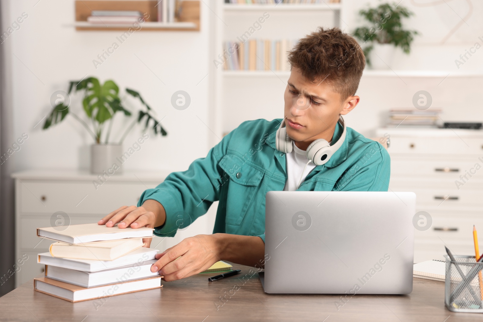 Photo of Student with headphones and books studying at wooden table indoors