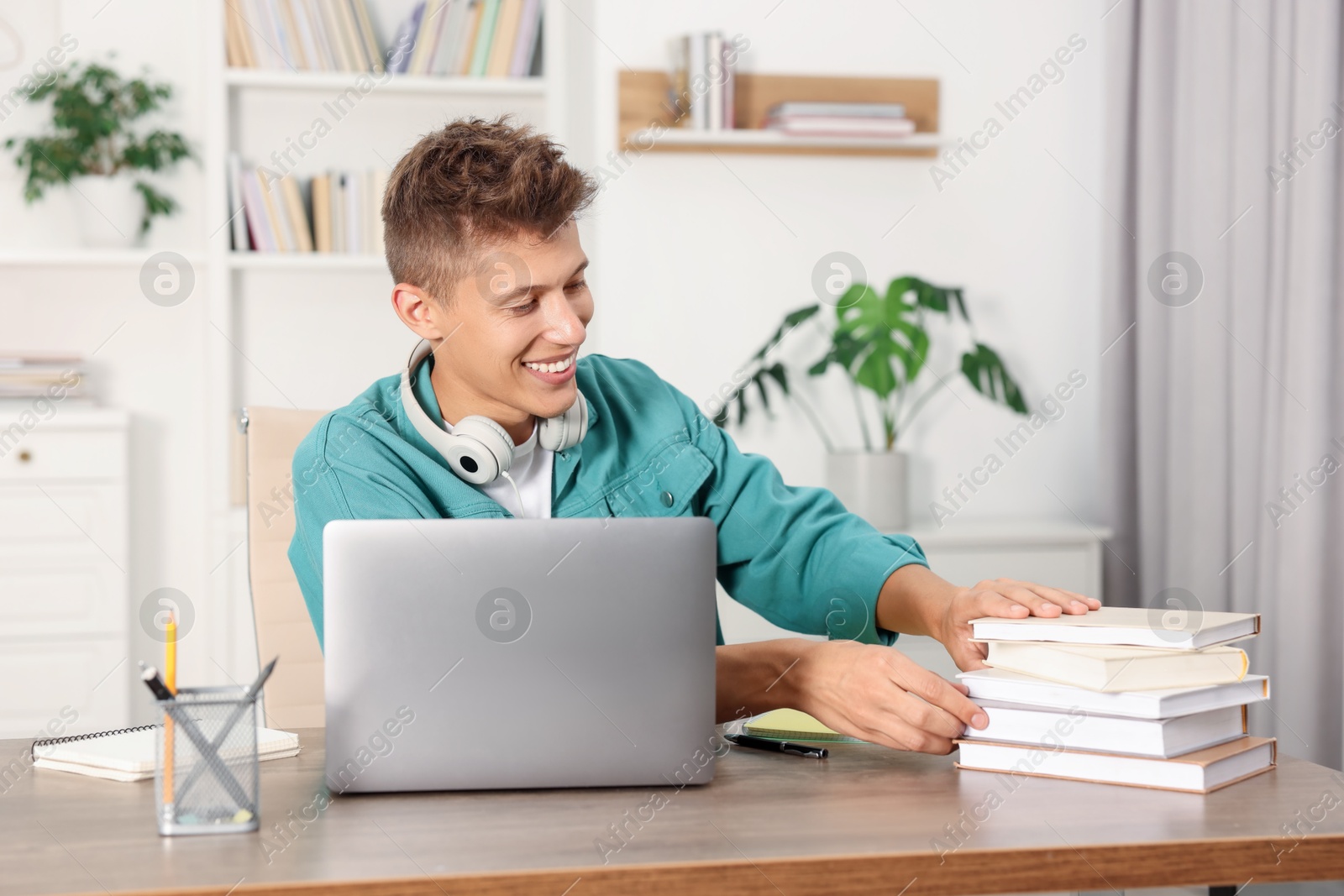 Photo of Student with headphones and books studying at wooden table indoors