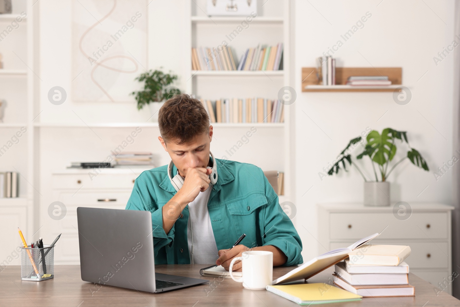 Photo of Student with headphones studying at table indoors