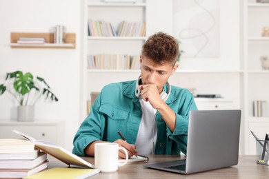 Student with headphones studying at wooden table indoors