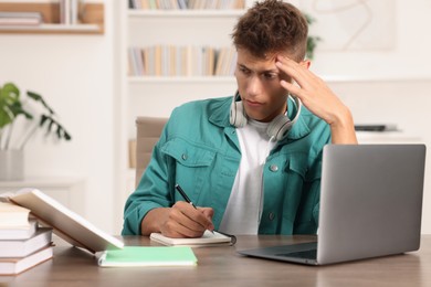 Photo of Student with headphones studying at wooden table indoors