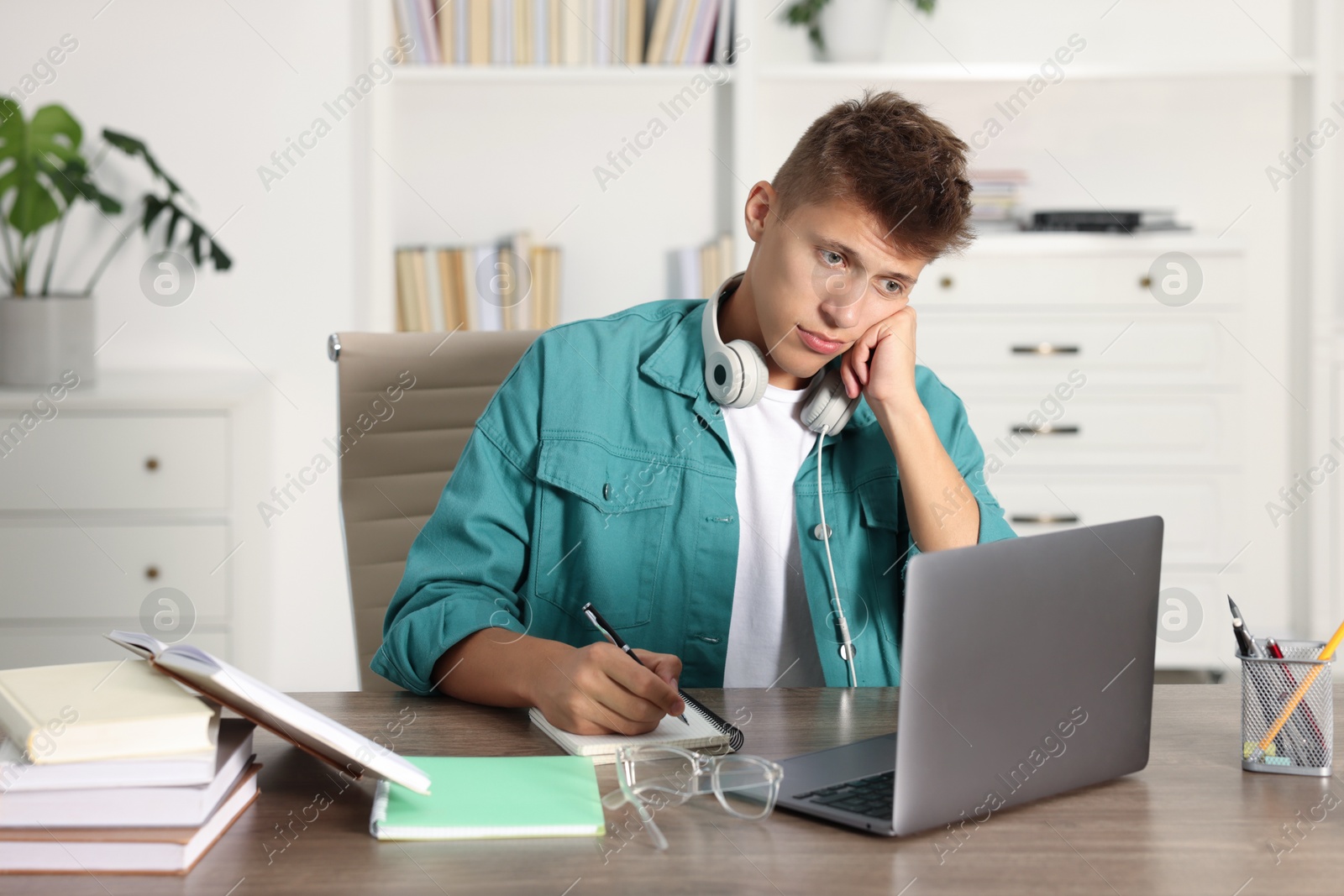 Photo of Student with headphones studying at wooden table indoors