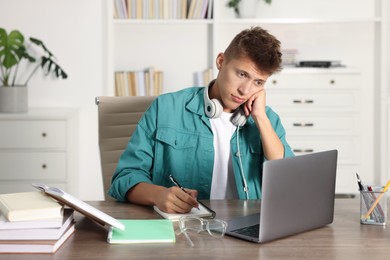 Student with headphones studying at wooden table indoors